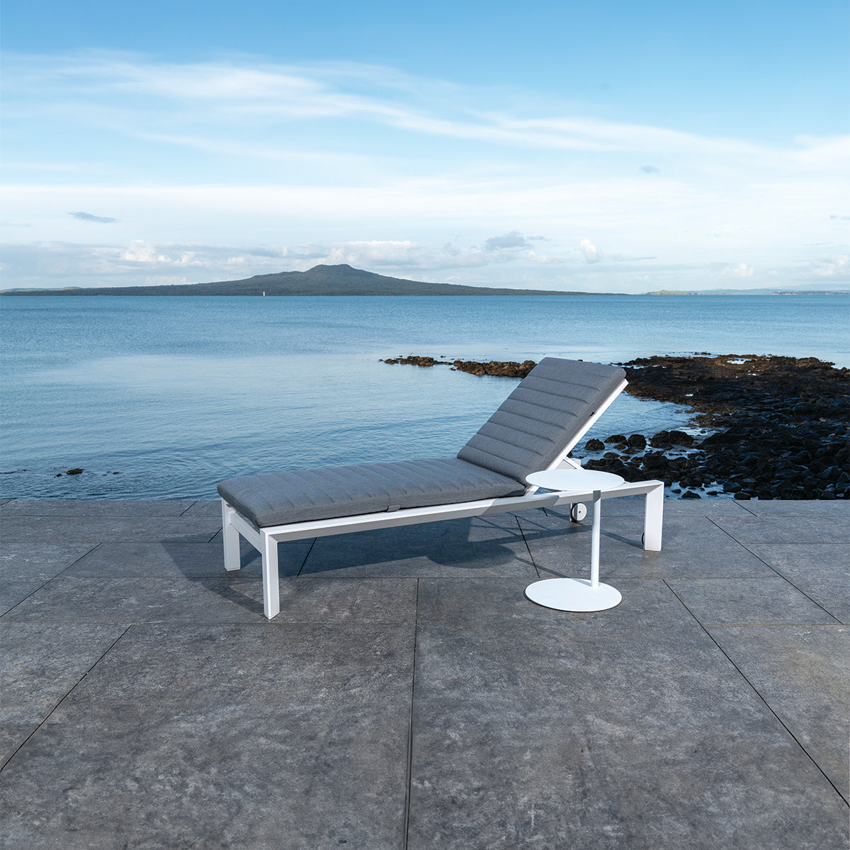 Amazon aluminium sun lounger in white with grey cushion in situ by beach patio.