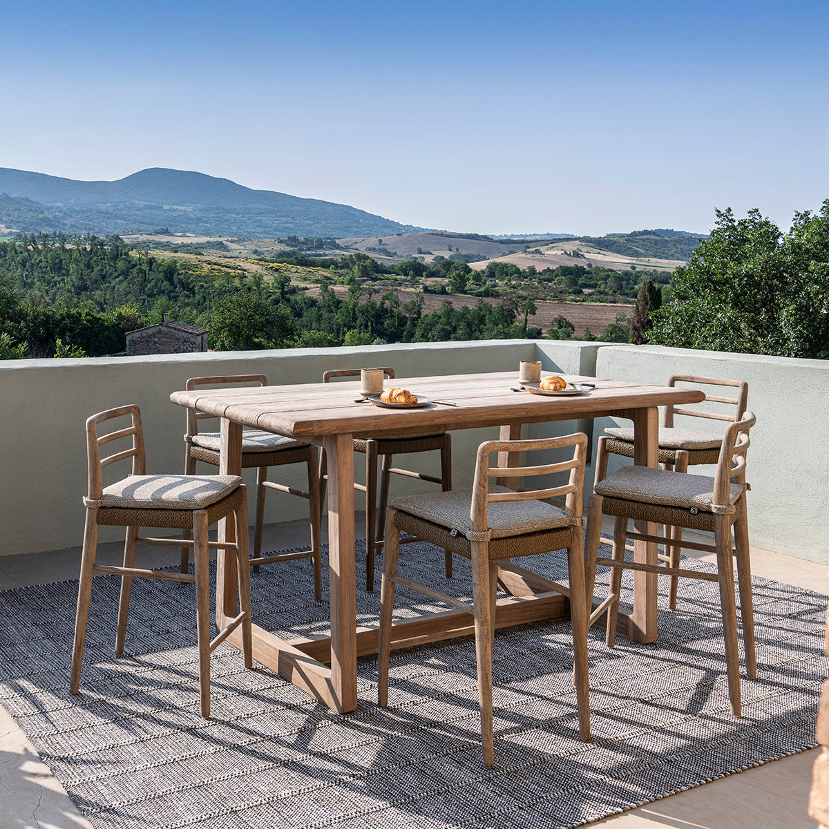 Donald outdoor reclaimed teak bar table with bar stools situated on deck overlooking hills