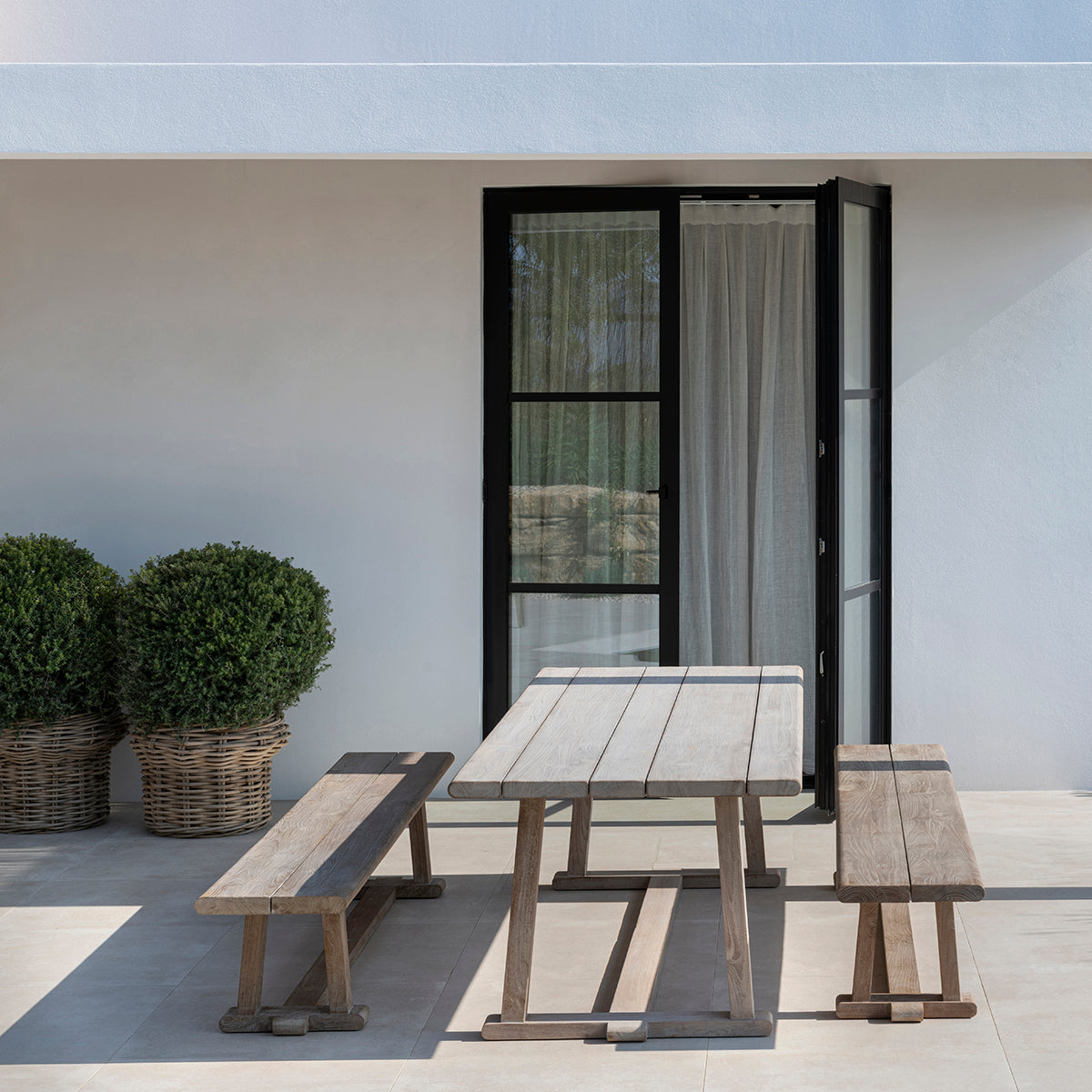 Outdoor dining set on patio including two benches and reclaimed teak dining table.