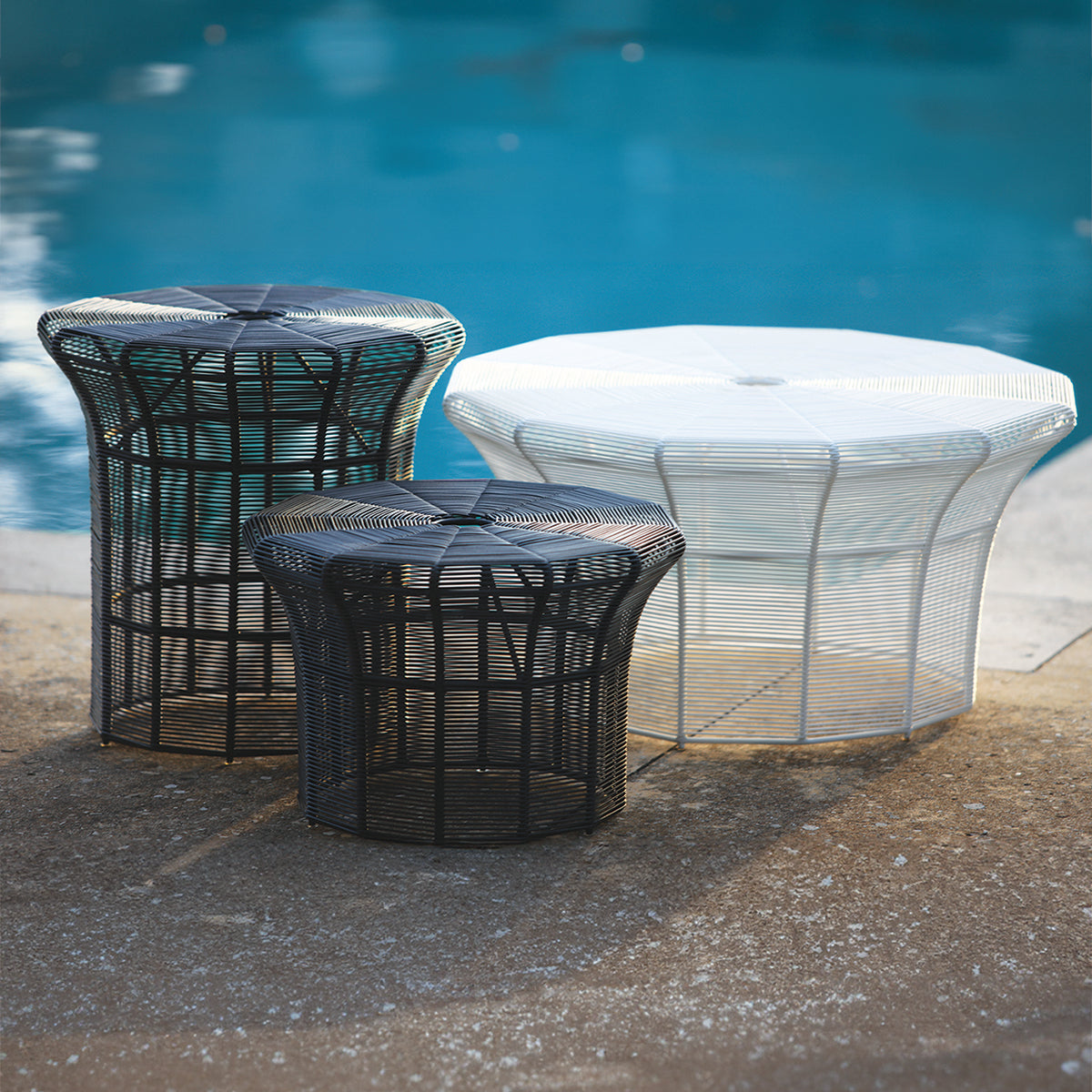 Three Poppi outdoor wicker woven dining tables in different sizes and colours poolside.