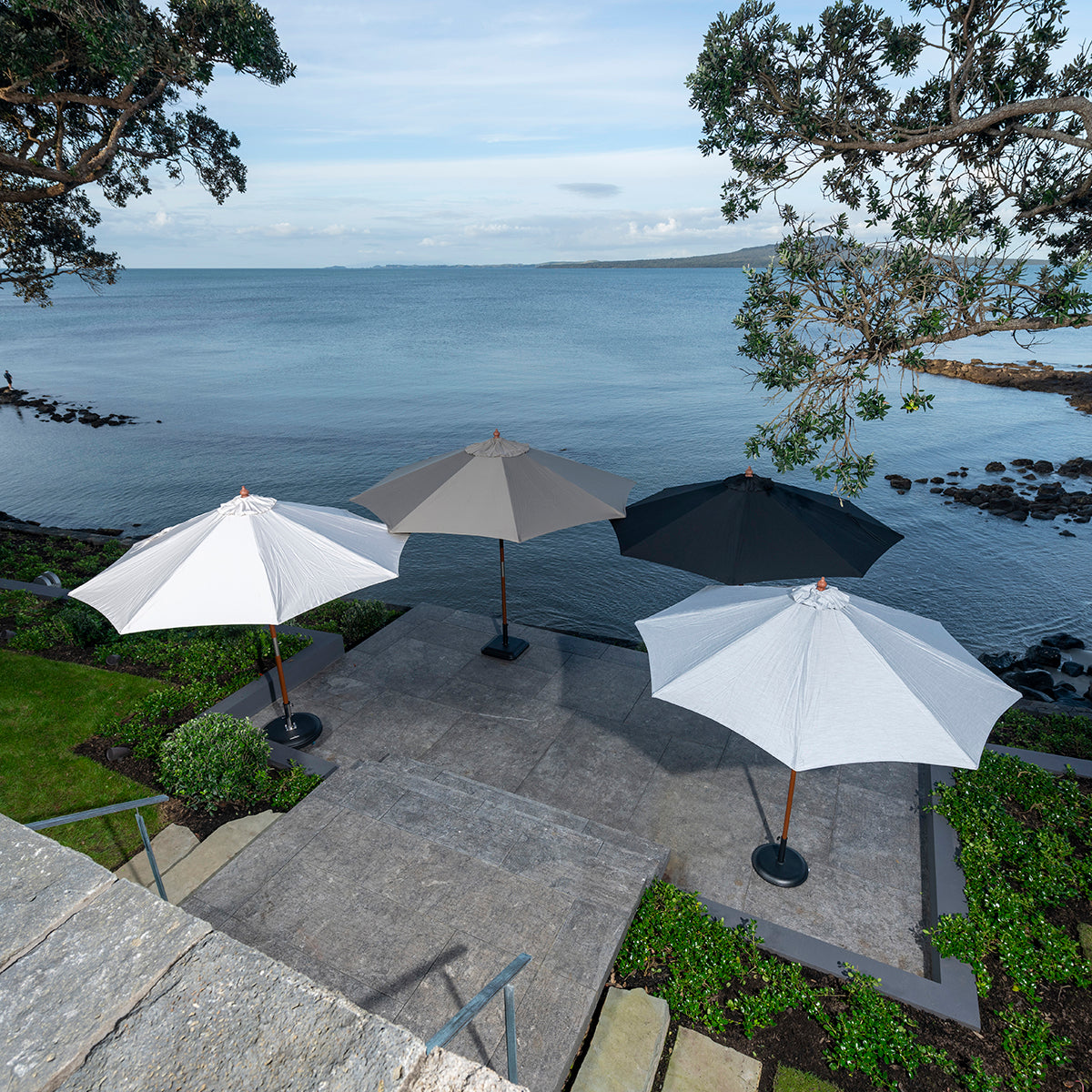 Group of four patio umbrellas in different colours set on patio of oceanfront property.