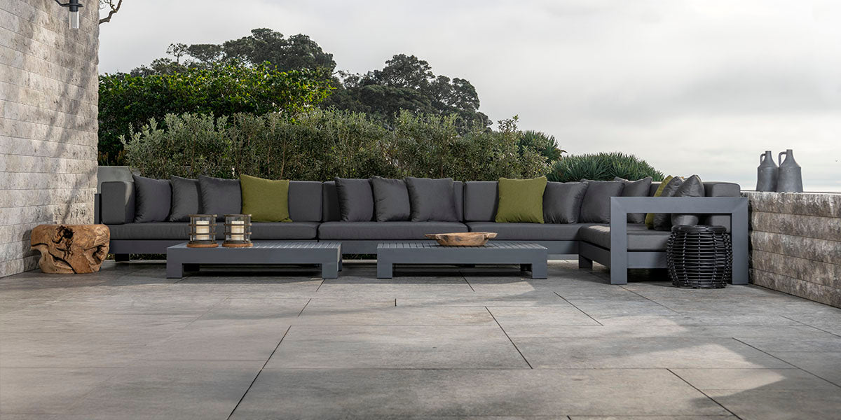 Outdoor patio furniture set with gray cushions on a stone patio.