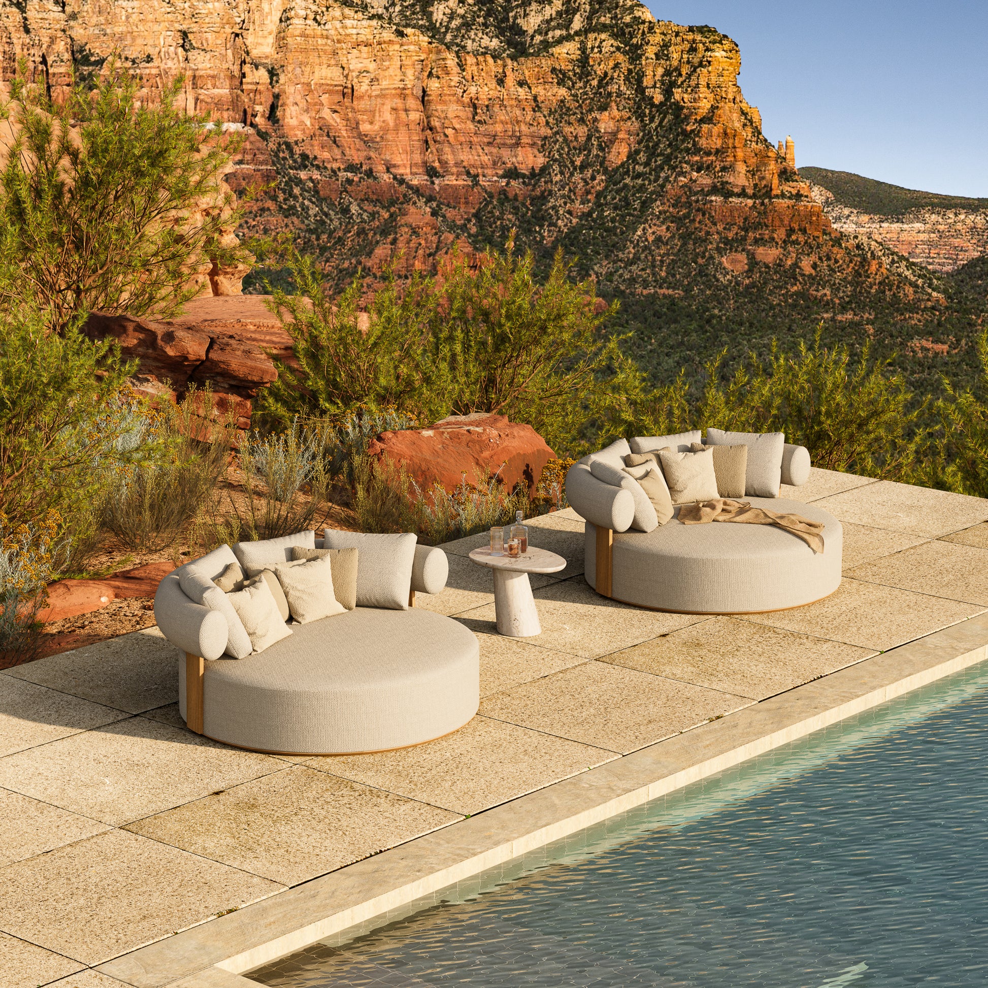 Two large round Cap Ferrat teak daybeds situated poolside. 