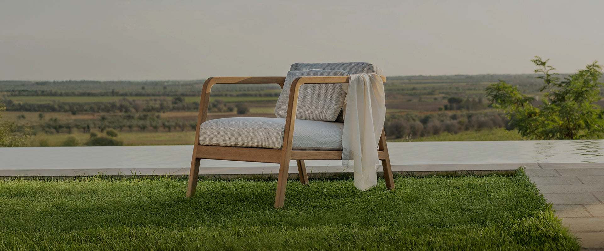 Sleek and elegant outdoor chair with a wooden frame and plush white cushions by Design Warehouse, showcasing premium outdoor furniture in NZ, including patio and garden furniture