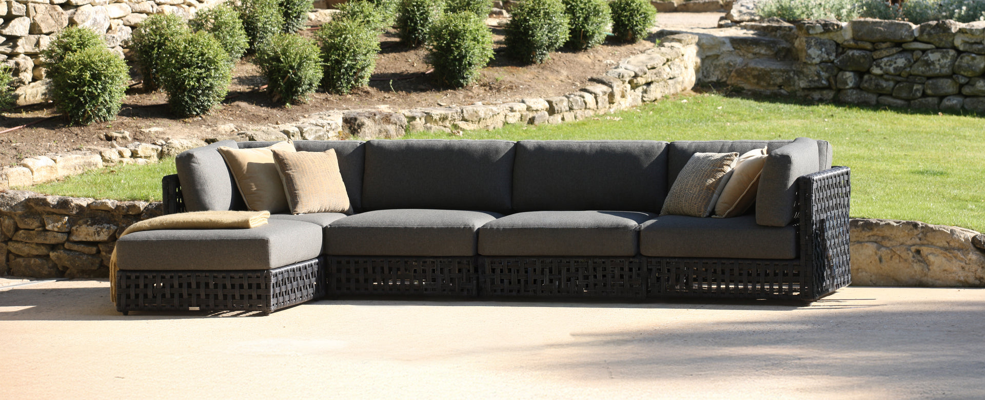 Outdoor patio sectional sofa with cushions on a patio area with greenery in the background